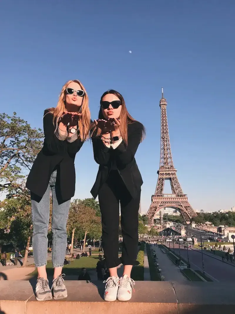 two women blowing kisses in front of Eiffel Tower
